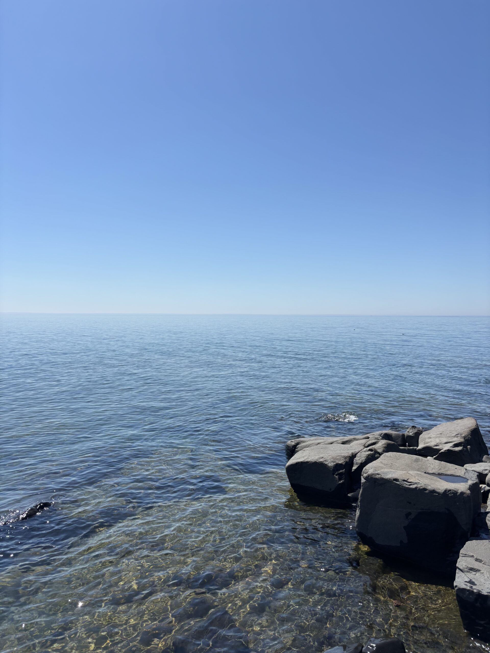 An open water view of Lake Superior, with rocks off to the bottom right-hand side of the page